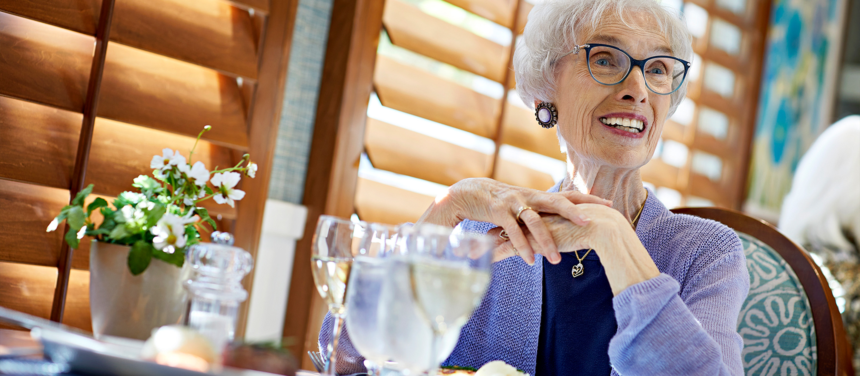 Smiling female resident seated in a dining room enjoys senior living in Orange County