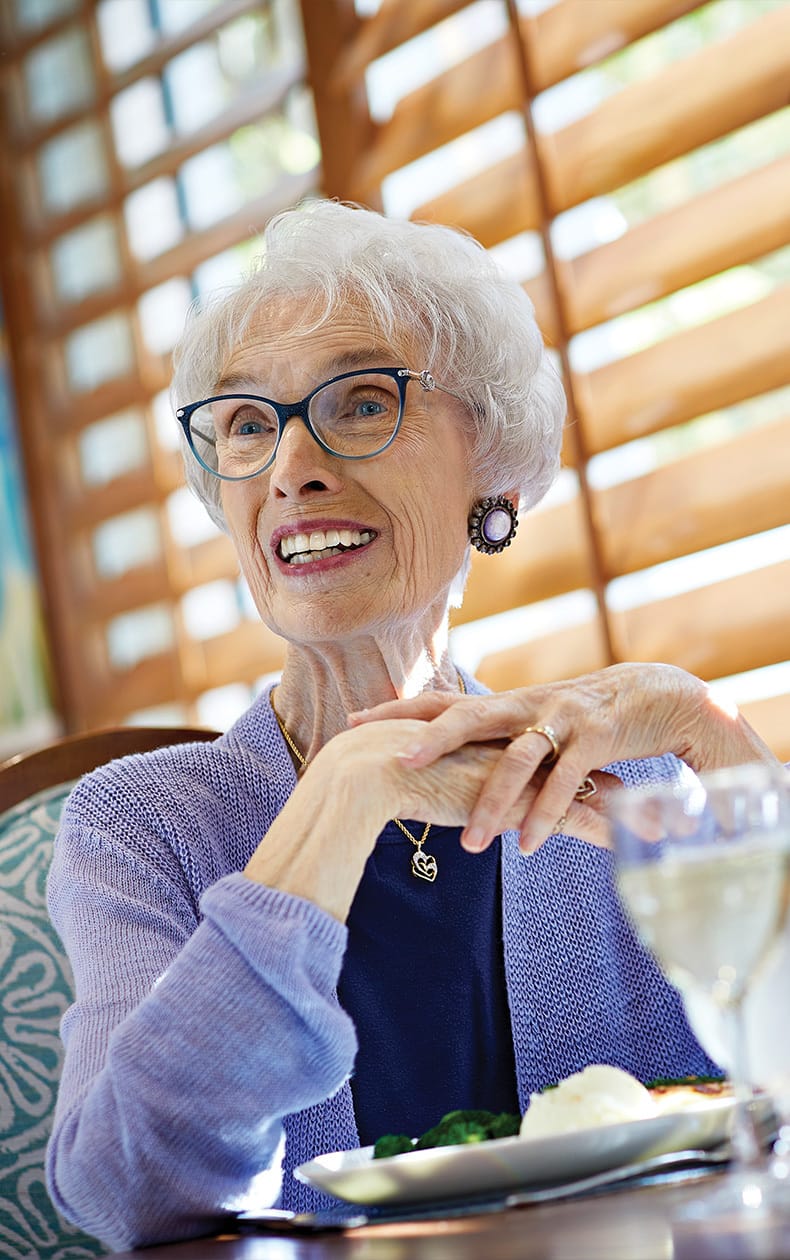 Smiling female resident seated in a dining room enjoys senior living in Orange County